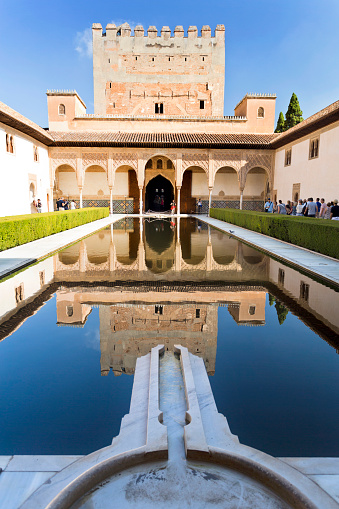 Granada, Spain – September 8, 2015: Tourists visiting the Court of the Myrtles with the south portico and Tower of Comares reflected on the central pool, in The Alhambra