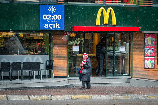 Istanbul, Turkey - January 18, 2016: Old lady is passing by McDonald's in Kadikoy, Istanbul in a snowy weather