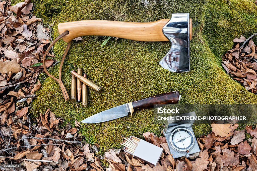Important items Above view of survival items placed on the grass with dry leaves around. An axe, hunting knife, compass, matchbox and some bullets are placed on the ground. Axe Stock Photo