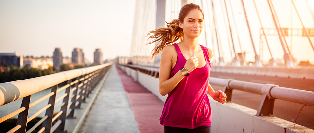 Female athlete running over the bridge early in the morning during her cardio routine. She has smart watch on her wrist.