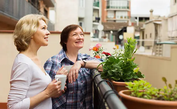 Two mature women drinking tea on balcony and smiling