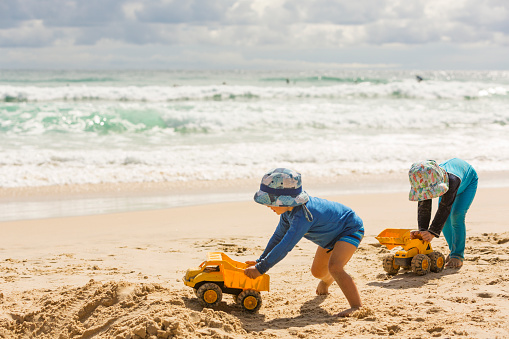 Boys at the beach wearing sun protection clothes while digging in the sand