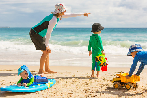 Mother and boys playing at the beach while wearing sun protection clothes