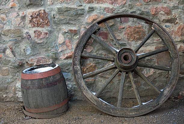 Old wooden wagon wheel and barrel on a stone wall in winter