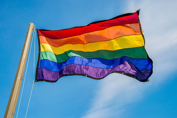 istock Gay rainbow flags waving over blue sky background 506904090