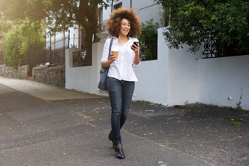 Portrait of young african american woman walking and looking at cellphone