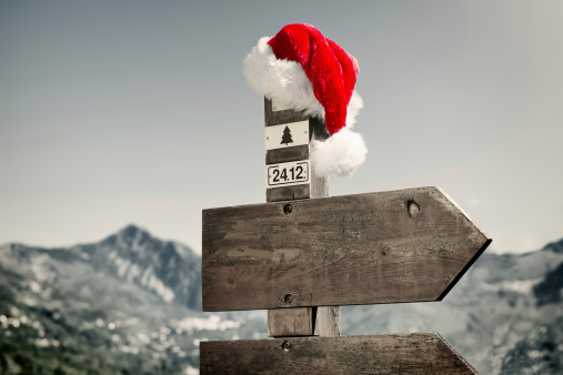 Signpost with Santa Hat in front of a mountain landscape. 