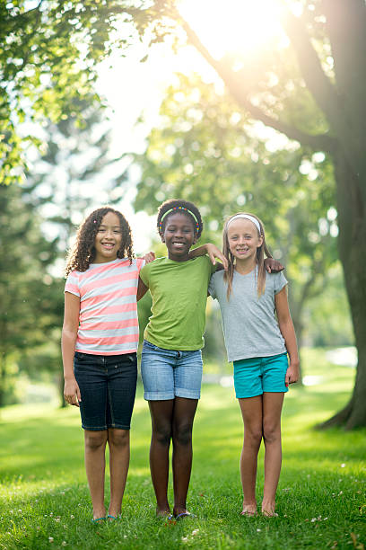 Adorable Afro mix race girl hold hand young sister and friend plan to play in park on holiday, primary school in private clothes stand in park on summer