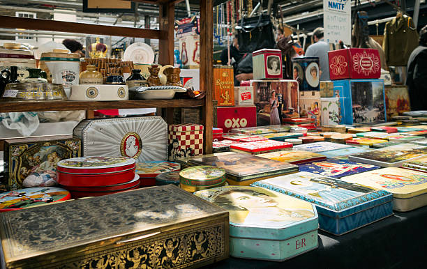 Greenwich, London, England - July 30, 2015: A large display of old tins, ashtrays and other collectables on a stall in a market in Greenwich, South London: many of the tins have a Royal theme. A few people can be seen in the background, looking at other stalls.