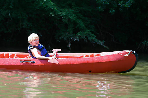 aktywne chłopiec korzystanie z kajaków na rzece w obóz letni - summer camp child teenager kayak zdjęcia i obrazy z banku zdjęć