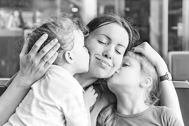 due figlie di madre felice di baciare loro - famiglia con due figli foto e immagini stock