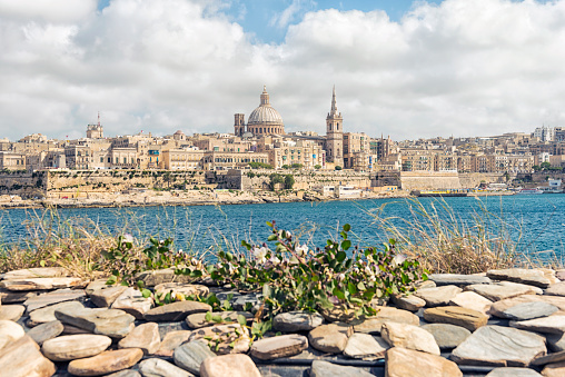 View on Valetta across the sea. The main focus on St. Paul Shipwrecked Church and Church of St. Catherine. In front view wall made of stones and flowers on the top. Scenic. Malta