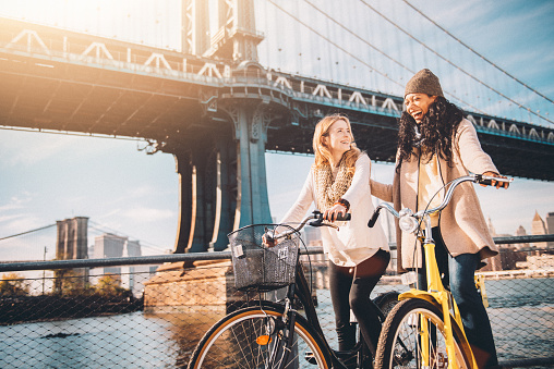 Two girl friends riding their bicycles along The East River in New York City.