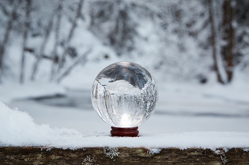 Winter scene with a transparent crystal ball reflecting the snowy landscape. Icy river appearing upside down on the ball.