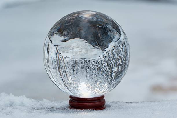 Winter scene with a transparent crystal ball reflecting the snowy landscape. Icy river appearing upside down on the ball.