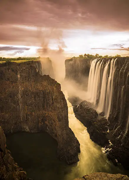 Victoria Falls is a waterfall in southern Africa on the Zambezi River at the border of Zambia and Zimbabwe. While it is neither the highest nor the widest waterfall in the world, it is classified as the largest, based on its width of 1,708 metres (5,604 ft) and height of 108 metres (354 ft), resulting in the world's largest sheet of falling water.