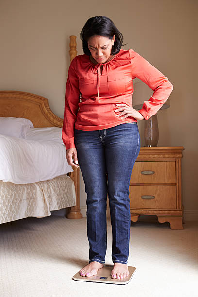 オーバーウェイト女性の表現に体重計のベッドルーム - mature adult sadness overweight women ストックフォトと画像