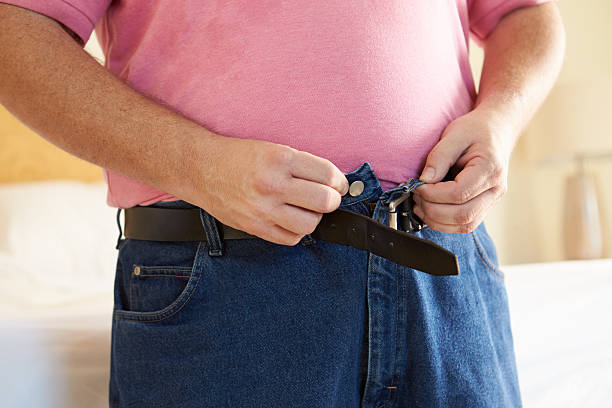 Close Up Of Overweight Man Trying To Fasten Trousers Close Up Of Overweight Man Trying To Fasten Trousers In Bedroom buttoning stock pictures, royalty-free photos & images