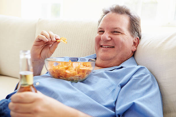 istock Overweight Man At Home Eating Chips And Drinking Beer 506934165