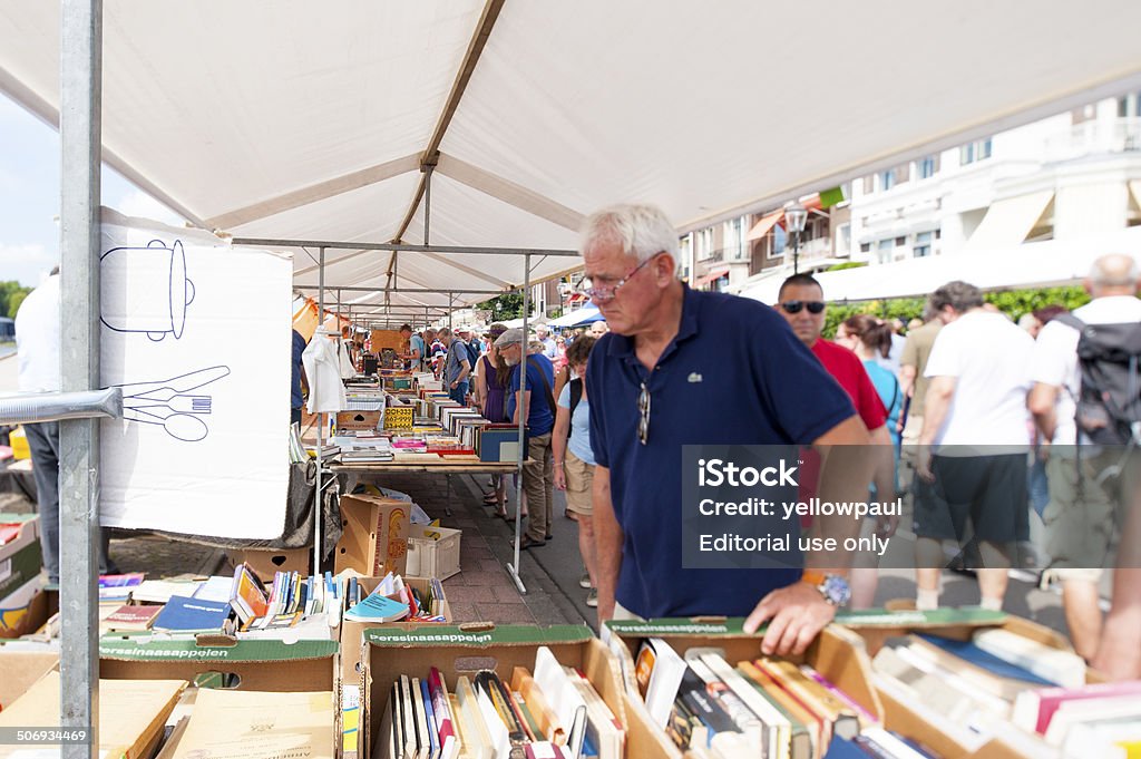 People shopping at white book stalls Deventer, the Netherlands - August 3, 2014: The book stand loaded with second hand books and the promenade crowded with people looking around the book stalls. Focal point is tilted and shifted at the row of books. Second Hand Sale Stock Photo