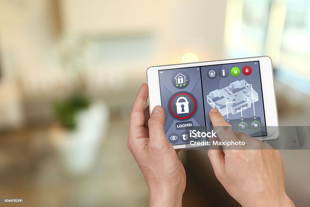 Smart home automation: locking house doors with security remote control Smart home automation: apartment interior with hand pointing an interactive tablet display showing house automatic locking system, with safety icons and symbols and unlocking functions. Burglar Alarm Stock Photo