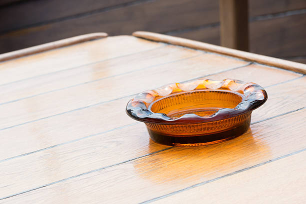 Orange glass ashtray on a boat's wooden table Orange glass ashtray on a wooden table rovinj harbor stock pictures, royalty-free photos & images