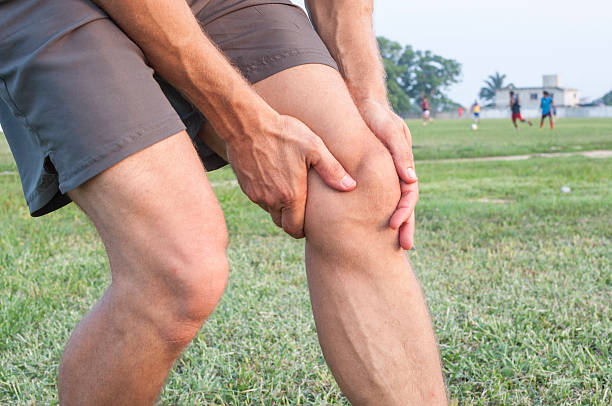 Knee injury Closeup of athletic Caucasian man holding his painful knee on soccer field hamstring stock pictures, royalty-free photos & images