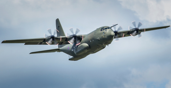 Duxford, UK - May 25, 2014: A Lockheed C130 Hercules military transport aircraft of the UK's Royal Air Force flies low over an air show in Cambridgeshire, England with its rear loading ramp lowered.