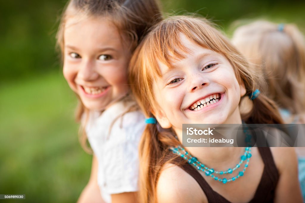 Three Happy Sisters Laughing While Sitting Together Outside Color stock photo of three happy little girls who are sisters sitting and laughing together outside. Child Stock Photo