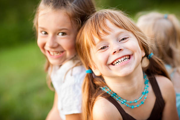 Three Happy Sisters Laughing While Sitting Together Outside Color stock photo of three happy little girls who are sisters sitting and laughing together outside. happy sibling day stock pictures, royalty-free photos & images