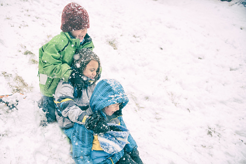 Three children sled quickly down a hill during a big snow storm