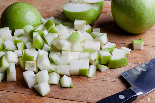 Cut granny smith green apples on wooden cutting board with knife from side
