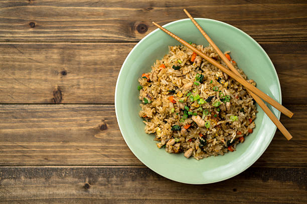 Fried Rice Top View on a Wooden Background Bowl of fried rice viewed from above with some chopsticks on the side. This asian inspired recipe uses lots of fresh ingredients like basil, carrots, onions and there's also fried eggs and chicken. fried rice stock pictures, royalty-free photos & images