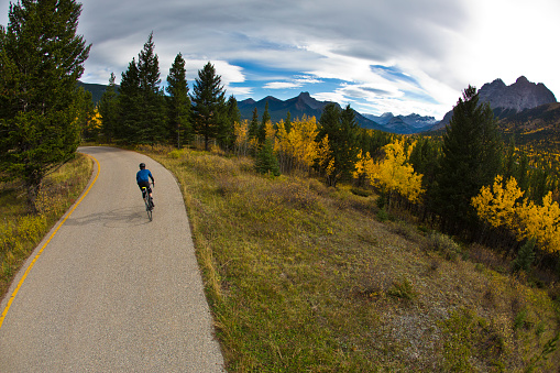 A male road bicyclist rides a quiet country lane in the Rocky Mountains of Canada in the fall.