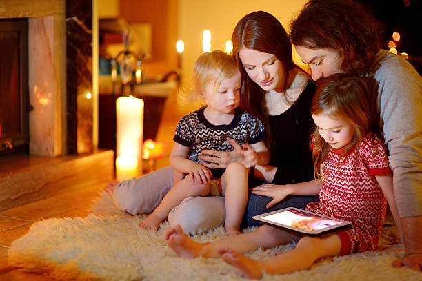 famille heureuse à l'aide d'une tablette pc avant une cheminée - luxury illuminated ornate christmas decoration photos et images de collection