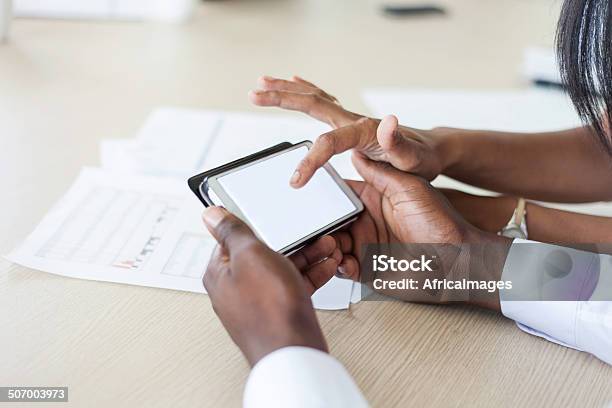 African Colleagues Looking At A Spread Sheet On A Cellphone Stock Photo - Download Image Now