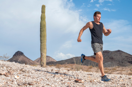 Muscular athletic male runner in shorts and running shoes runs across rocky barren desert terrain