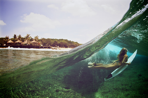 A above and below view of a girl duck diving a wave in the tropics.