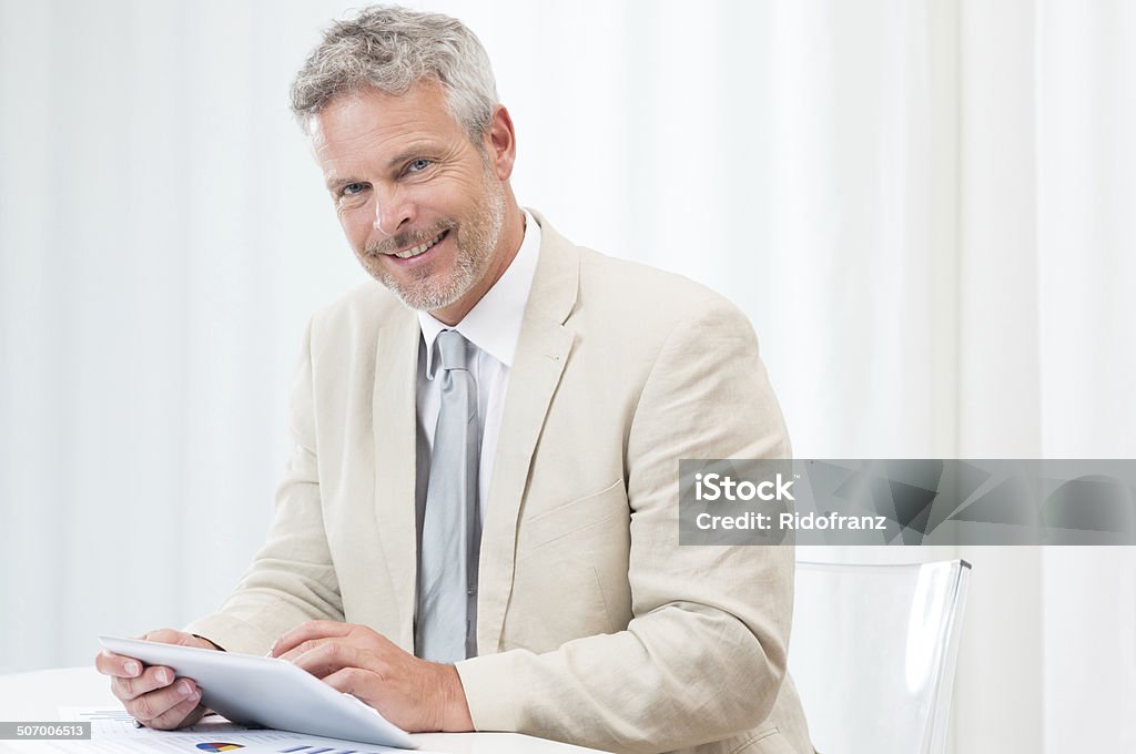 Happy Mature Businessman With Tablet Happy Mature Businessman Looking At Camera And Using Laptop At Workplace 40-49 Years Stock Photo