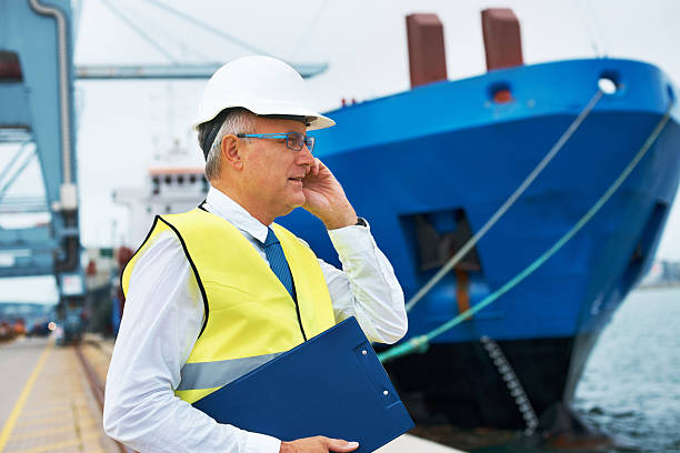 Let's secure that cargo for the departure... A dock worker standing at the harbor amidst shipping industry activity while taking a call on his mobile customs official photos stock pictures, royalty-free photos & images