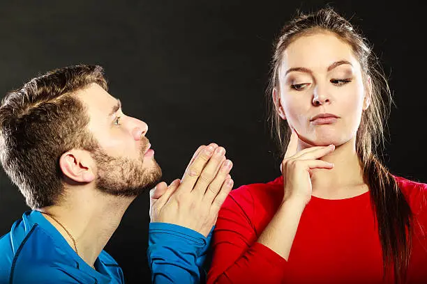 Husband apologizing wife. Man asking woman for forgivness. Boyfriend trying to convince girlfriend. Conflicted couple in studio on black. Relationship problem.