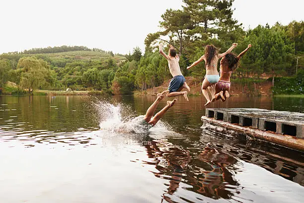 Shot of a group of teenage friends jumping off a pier into a lake