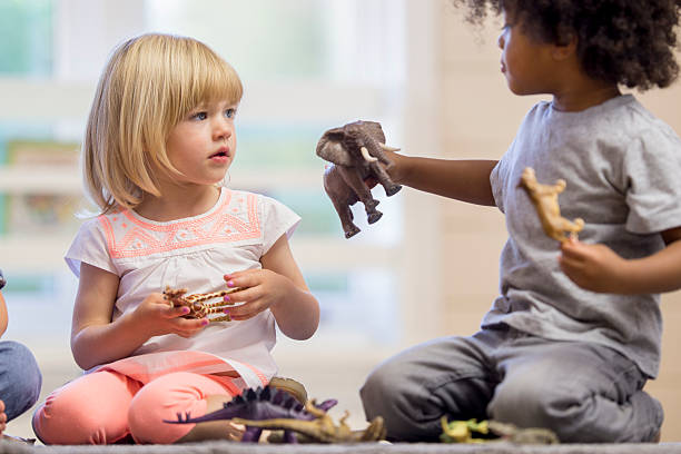 Sharing Toys A multi-ethnic group of elementary age children are playing together with plastic animal toys at day care. preschool building photos stock pictures, royalty-free photos & images