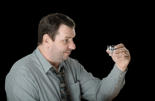 Unshaven mature man posing with vodka shot on black background