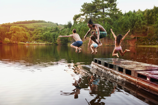 Shot of a group of teenage friends jumping off a pier into a lake