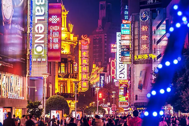 Crowds walk below neon signs on Nanjing Road. The street is the main shopping district of the city and one of the world's busiest shopping districts. 