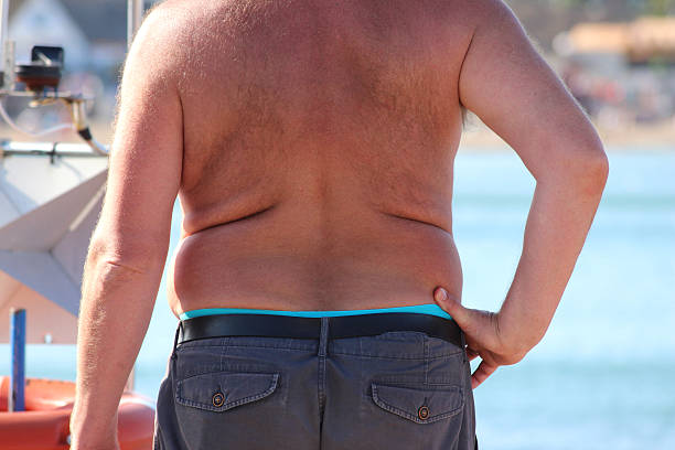 Overweight topless man at seaside, fat man image / beer belly Photo of an overweight topless, fat man at the seaside / beach, showing his beer belly / muffin top as he enjoys some summer sunshine. fat guy no shirt stock pictures, royalty-free photos & images