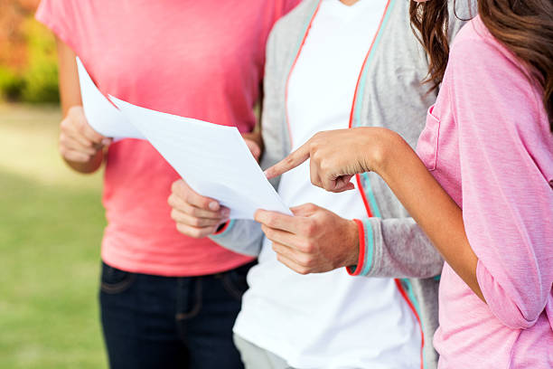 Girl Pointing At Test Result While Standing With Students Midsection of teenage girl pointing at test result while standing with students in university campus. Horizontal shot. educational test results stock pictures, royalty-free photos & images