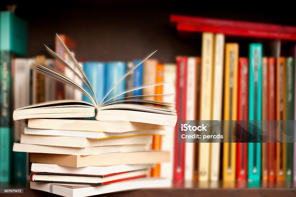 Stack of books on a shelf, multicolored book spines. Stack of books on a wooden library shelf, one of them open on top, multicolored book spines background. Book Stock Photo