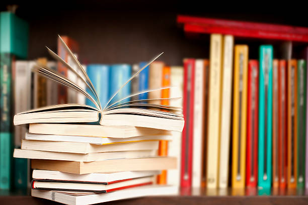 Stack of books on a shelf, multicolored book spines. Stack of books on a wooden library shelf, one of them open on top, multicolored book spines background. textbook stock pictures, royalty-free photos & images